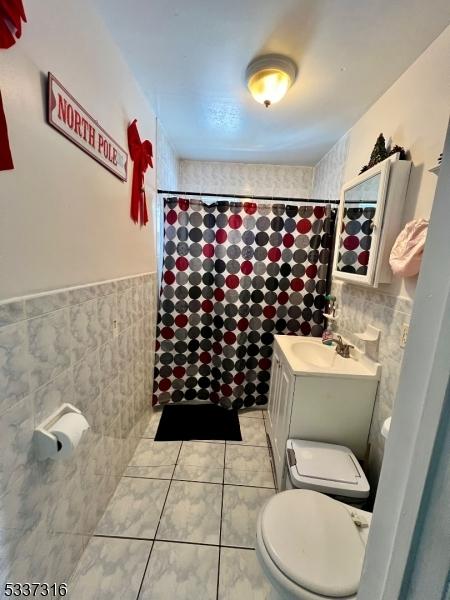 bathroom with tile walls, tile patterned flooring, a shower with shower curtain, vanity, and toilet