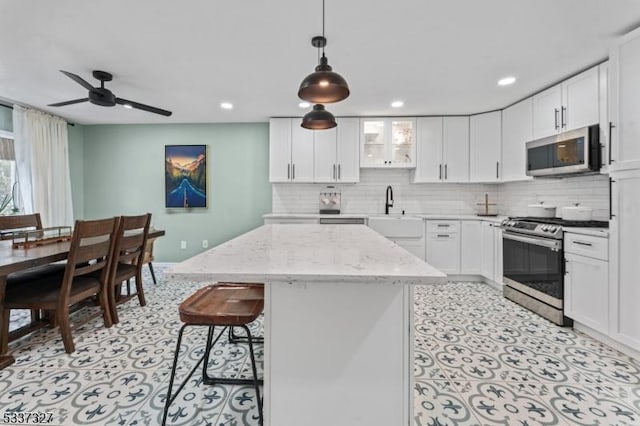 kitchen featuring pendant lighting, appliances with stainless steel finishes, white cabinetry, a center island, and light stone countertops