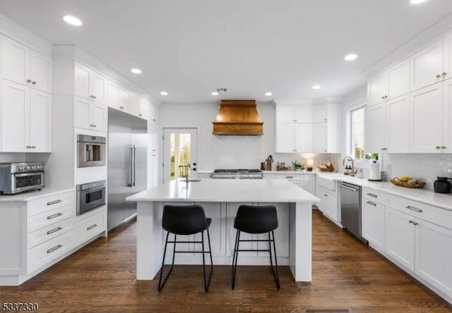 kitchen featuring premium range hood, appliances with stainless steel finishes, a kitchen breakfast bar, white cabinets, and a kitchen island