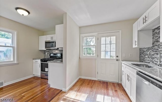 kitchen with sink, stainless steel appliances, white cabinetry, and light hardwood / wood-style floors