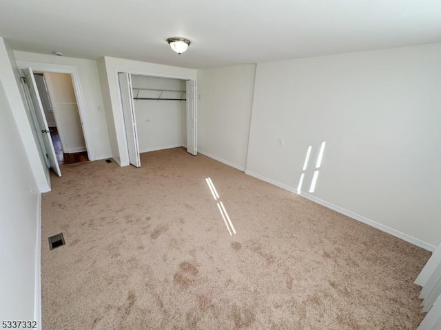 unfurnished bedroom with light colored carpet and a closet