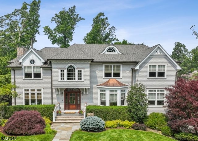 shingle-style home with a shingled roof, a chimney, and a front lawn