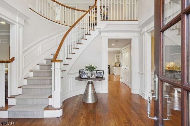 entrance foyer featuring crown molding, dark wood-style flooring, a towering ceiling, and a decorative wall