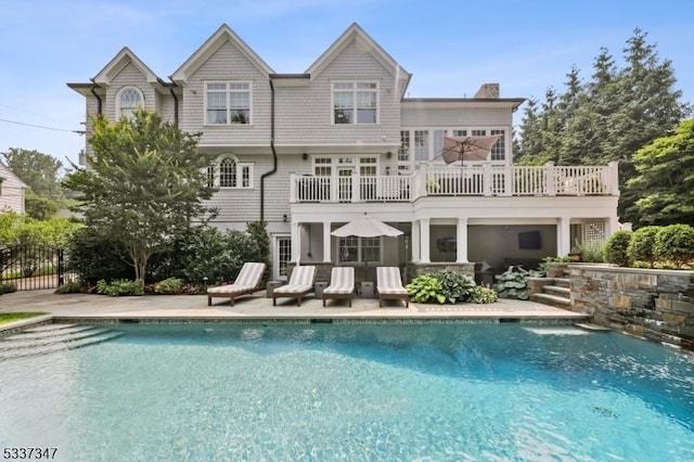 rear view of house with a chimney, a patio area, fence, a balcony, and an outdoor pool