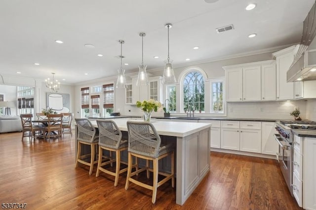 kitchen featuring stainless steel stove, white cabinetry, hanging light fixtures, and a large island