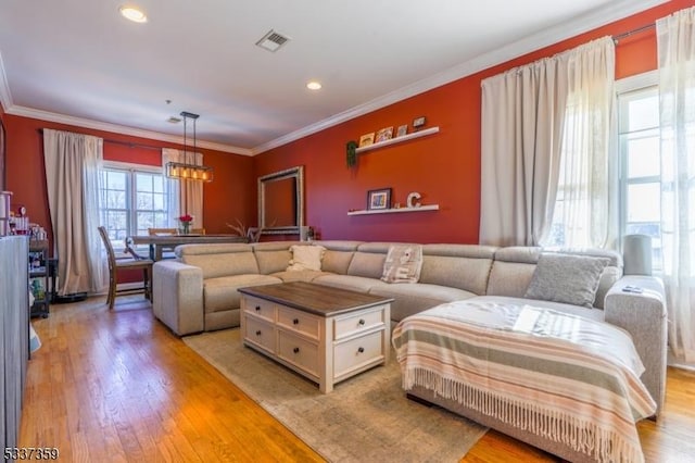 living room with light wood finished floors, visible vents, an inviting chandelier, and ornamental molding