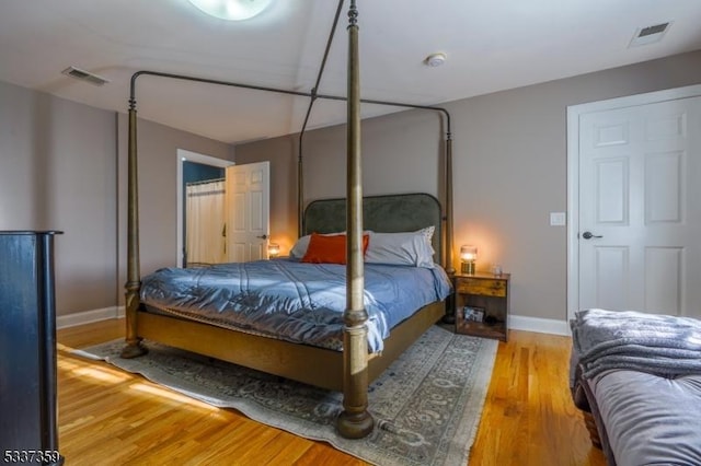 bedroom with baseboards, visible vents, and wood finished floors