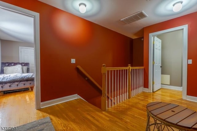 corridor with baseboards, visible vents, wood finished floors, and an upstairs landing