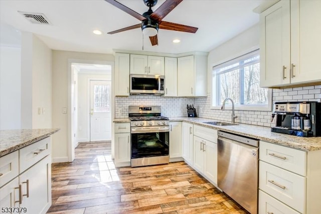 kitchen with sink, white cabinetry, stainless steel appliances, light stone counters, and light hardwood / wood-style floors