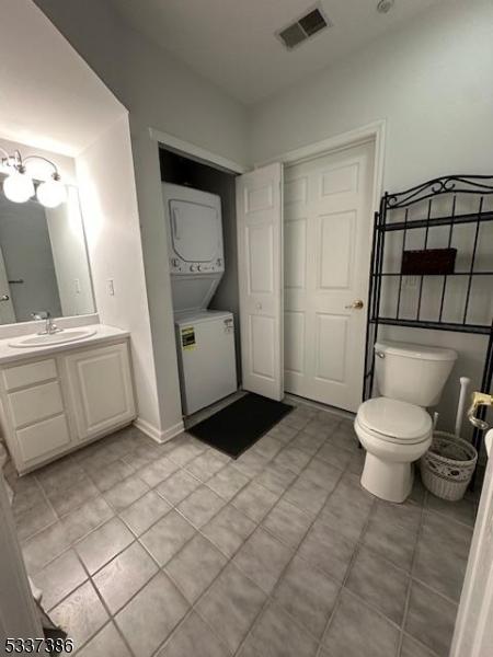 bathroom featuring stacked washer and dryer, vanity, tile patterned floors, and toilet