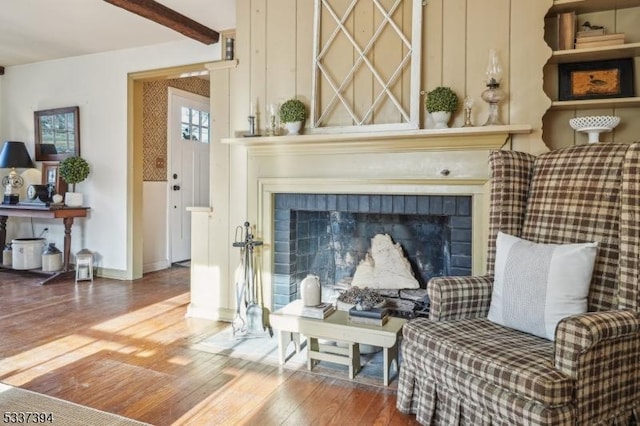 living area featuring a brick fireplace, wood-type flooring, baseboards, and beam ceiling