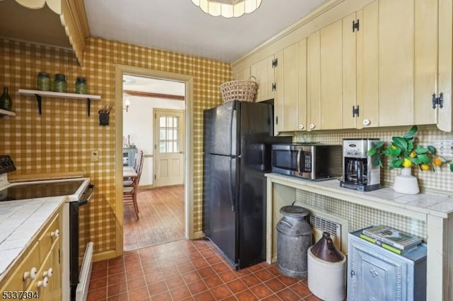 kitchen featuring dark tile patterned flooring, tile counters, decorative backsplash, black appliances, and wallpapered walls