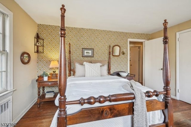 bedroom with wallpapered walls, an accent wall, baseboards, and wood finished floors