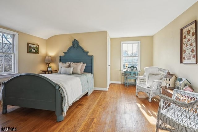 bedroom featuring light wood-type flooring, lofted ceiling, and baseboards