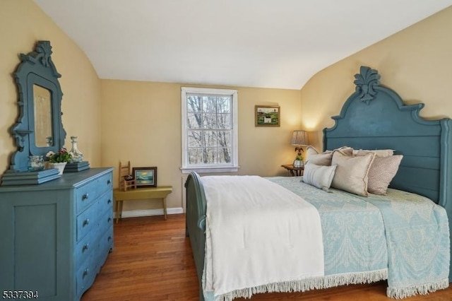 bedroom with vaulted ceiling, wood finished floors, and baseboards