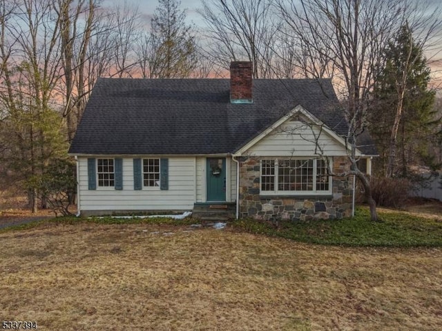 cape cod-style house featuring entry steps, stone siding, a lawn, and a chimney