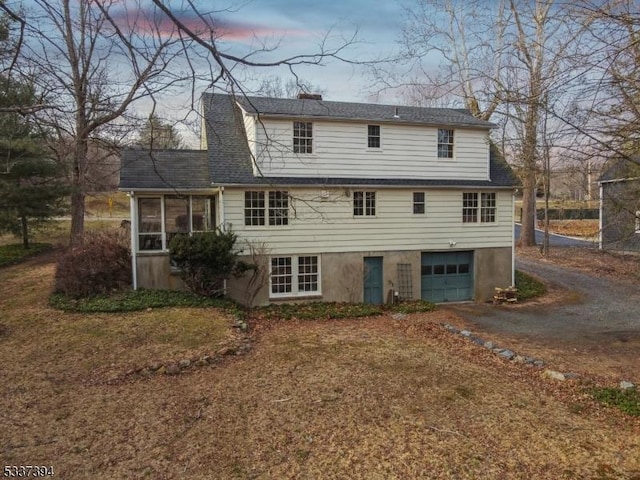 rear view of house featuring a garage, a sunroom, and dirt driveway