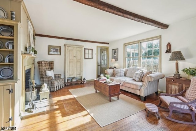 living area featuring hardwood / wood-style floors, a fireplace, ornamental molding, and beamed ceiling