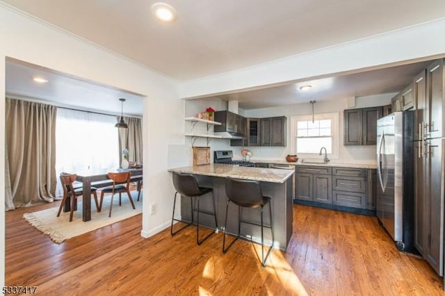 kitchen with hardwood / wood-style floors, appliances with stainless steel finishes, pendant lighting, a kitchen breakfast bar, and kitchen peninsula