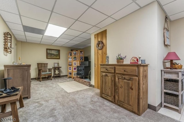 sitting room with light carpet, a paneled ceiling, and a wood stove