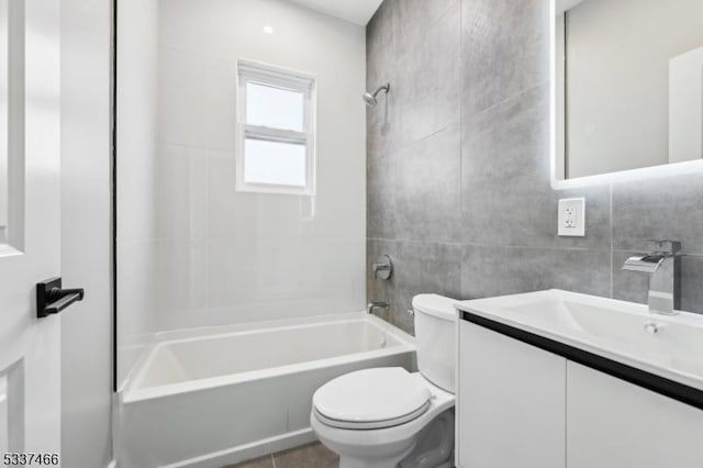 full bathroom with vanity, toilet, tiled shower / bath combo, and tile walls