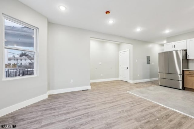 kitchen with stainless steel refrigerator, white cabinetry, electric panel, and light wood-type flooring