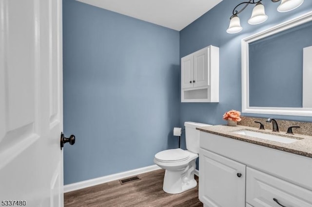 bathroom with toilet, wood finished floors, visible vents, vanity, and baseboards