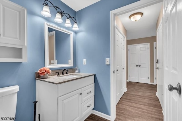 half bathroom featuring toilet, wood finished floors, vanity, and baseboards