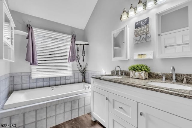 full bathroom featuring wood finished floors, vaulted ceiling, a sink, and double vanity