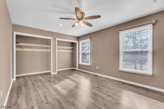 unfurnished bedroom featuring multiple closets, ceiling fan, light wood finished floors, and baseboards