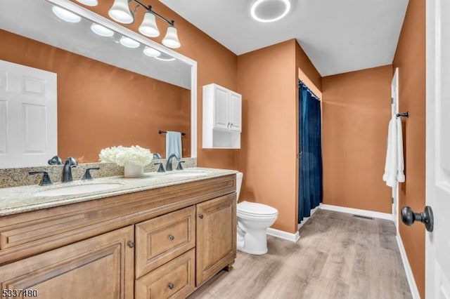 bathroom with double vanity, wood finished floors, a sink, and baseboards