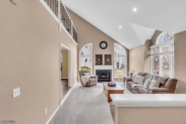 living room featuring a warm lit fireplace, high vaulted ceiling, light colored carpet, recessed lighting, and baseboards