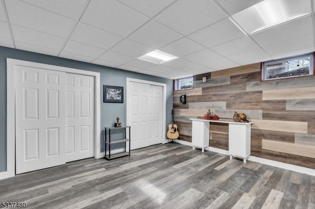 finished basement featuring a paneled ceiling, wooden walls, baseboards, and wood finished floors