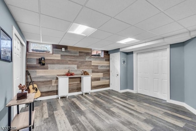 finished basement with an accent wall, wood walls, wood finished floors, a drop ceiling, and baseboards