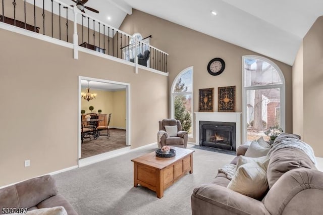 living area featuring a fireplace with flush hearth, a wealth of natural light, light colored carpet, and ceiling fan with notable chandelier