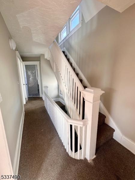 staircase with carpet floors, a textured ceiling, and baseboards