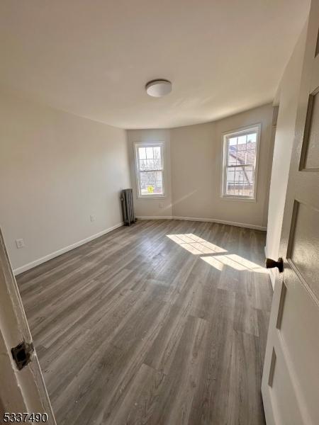 spare room with radiator, baseboards, and dark wood finished floors