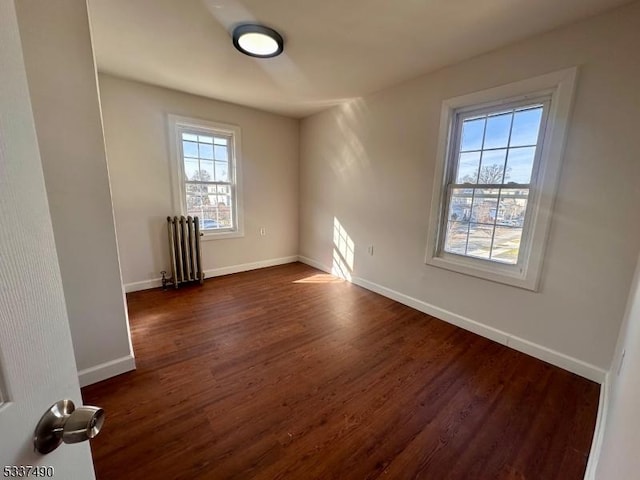 unfurnished room featuring dark wood-style floors, baseboards, and radiator heating unit