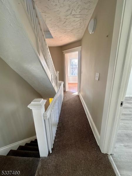 hall with stairway, carpet flooring, a textured ceiling, and baseboards