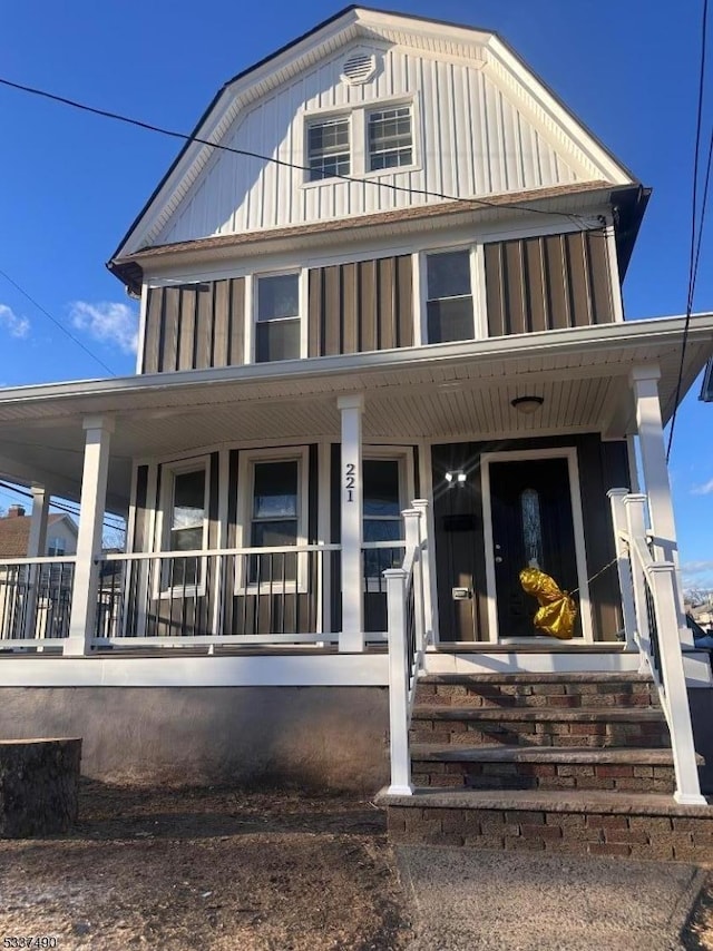 view of front facade with covered porch, board and batten siding, and a gambrel roof