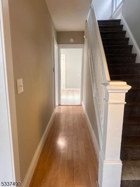 corridor with stairs, wood finished floors, and baseboards