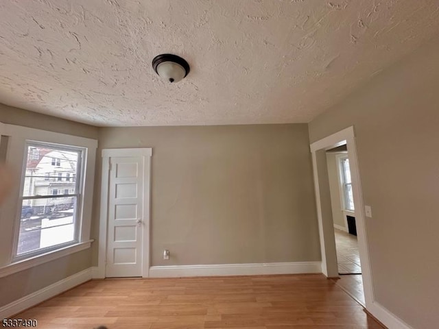 spare room with baseboards, a textured ceiling, and light wood finished floors