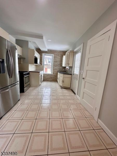 kitchen with light tile patterned floors, dark countertops, appliances with stainless steel finishes, a sink, and under cabinet range hood