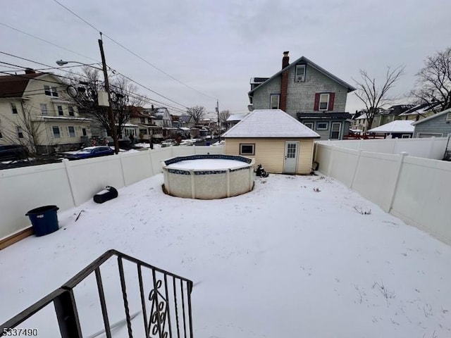 snowy yard with a residential view, a fenced backyard, an outdoor pool, and an outbuilding