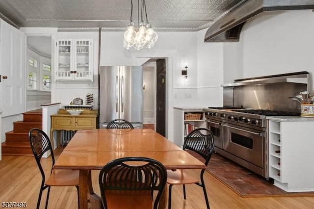 kitchen with white cabinetry, stainless steel appliances, decorative light fixtures, light hardwood / wood-style floors, and range hood