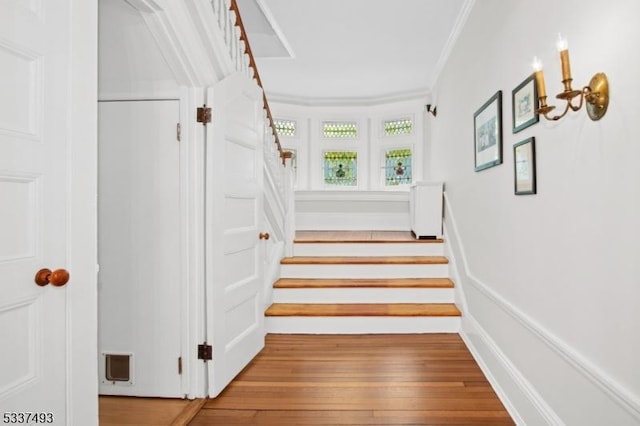 stairway with crown molding and wood-type flooring