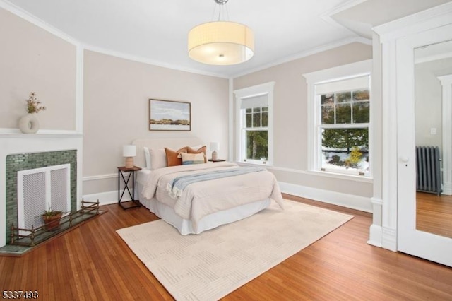 bedroom featuring ornamental molding, radiator, a tiled fireplace, and wood-type flooring