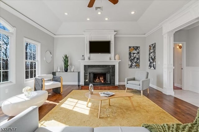 living room featuring dark hardwood / wood-style floors, ceiling fan, a fireplace, a tray ceiling, and ornate columns