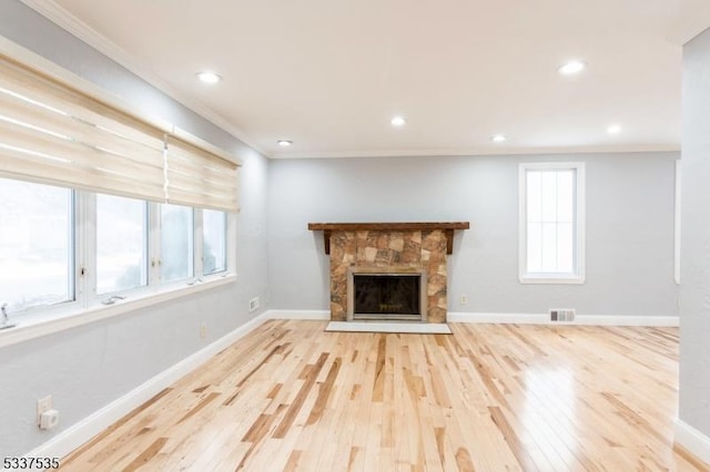 unfurnished living room with light hardwood / wood-style flooring, a stone fireplace, and crown molding