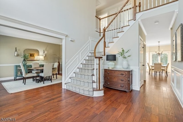 staircase featuring an inviting chandelier, ornamental molding, a decorative wall, and wood finished floors